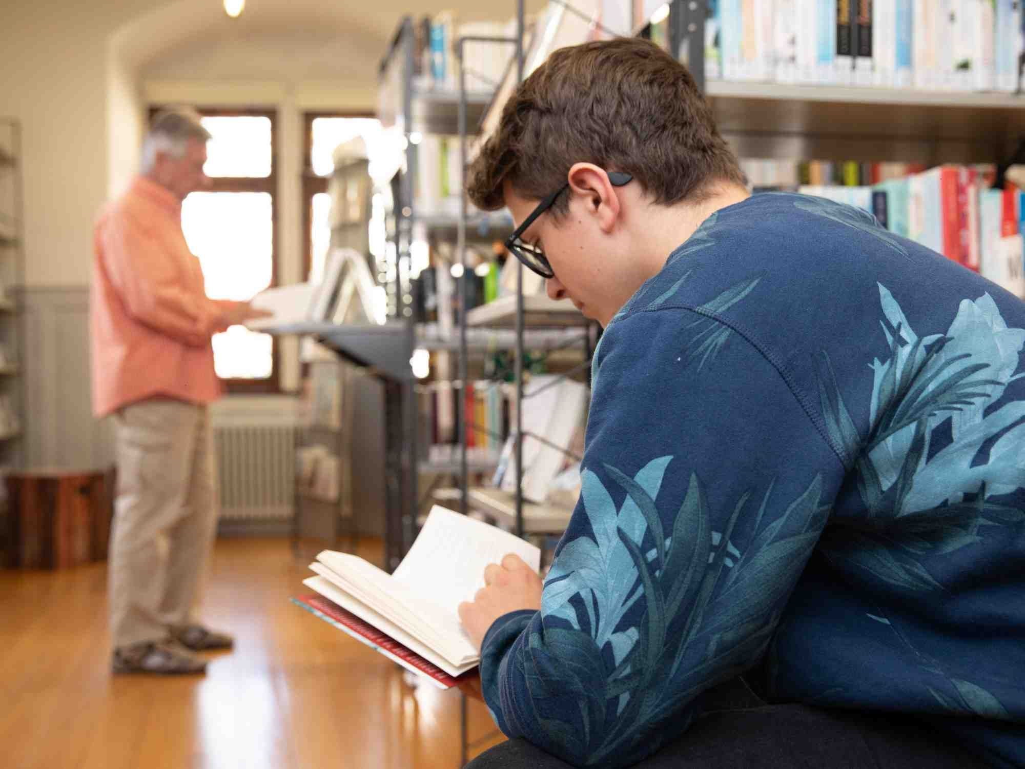 Stadtbücherei_Selbstausleihe_Text_2000x1555px Ein junger Mann sitzt in der Stadtbücherei und liest ein Buch.